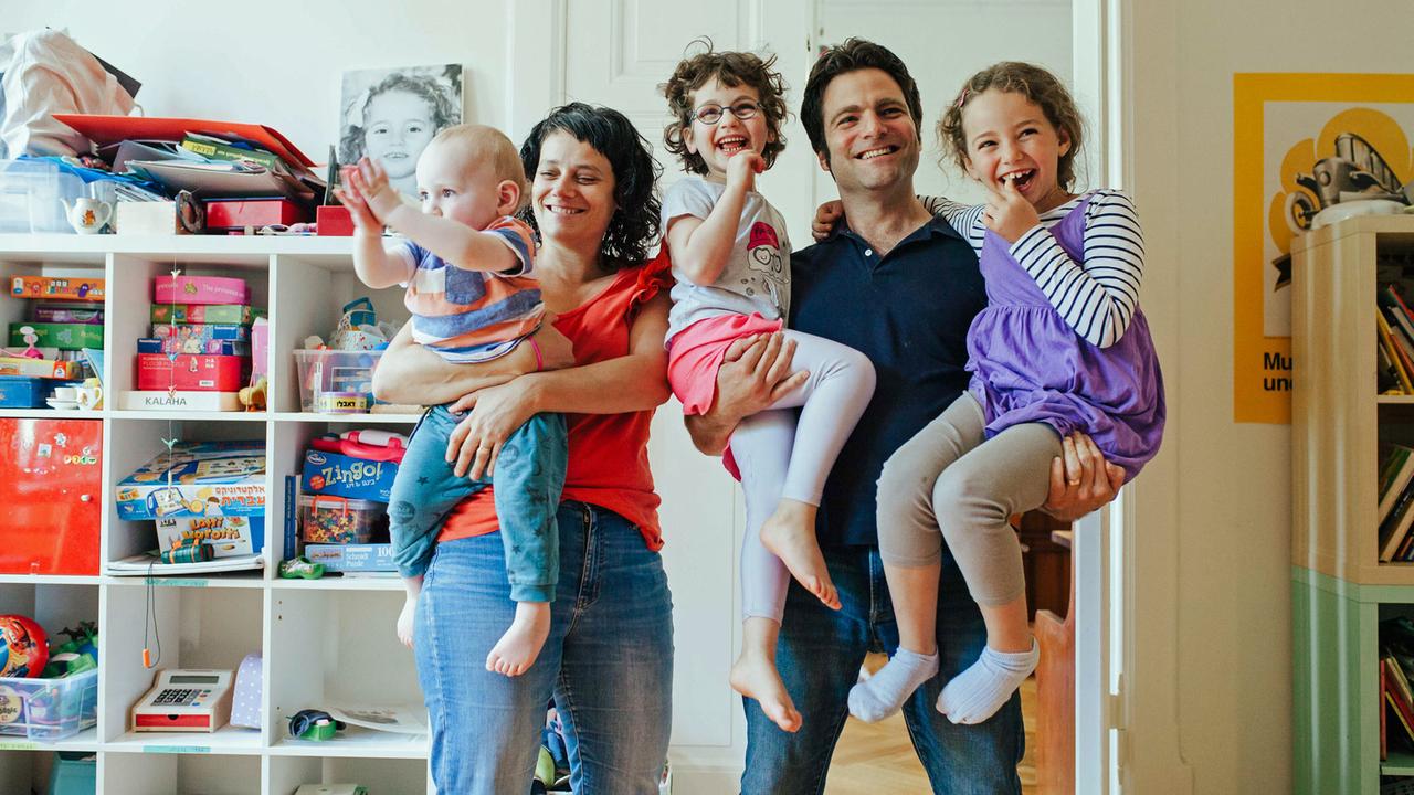 Ofer und Gili Waldman in ihrer Berliner Wohnung. Gili trägt den jüngsten Sohn Jonathan auf dem Arm, Ofer die beiden Töchter Ori und Naama.