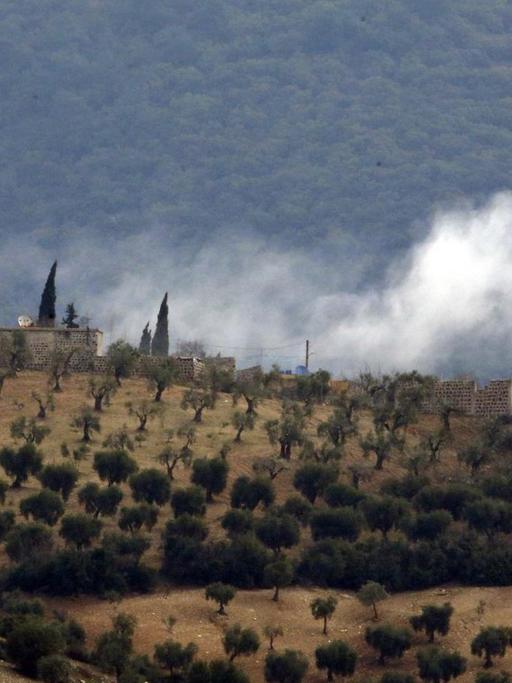 Das Bild zeigt Rauch, der über einer hügeligen Landschaft im Nordwesten Syriens nach Artilleriebeschuss durch die türkische Armee aufsteigt.