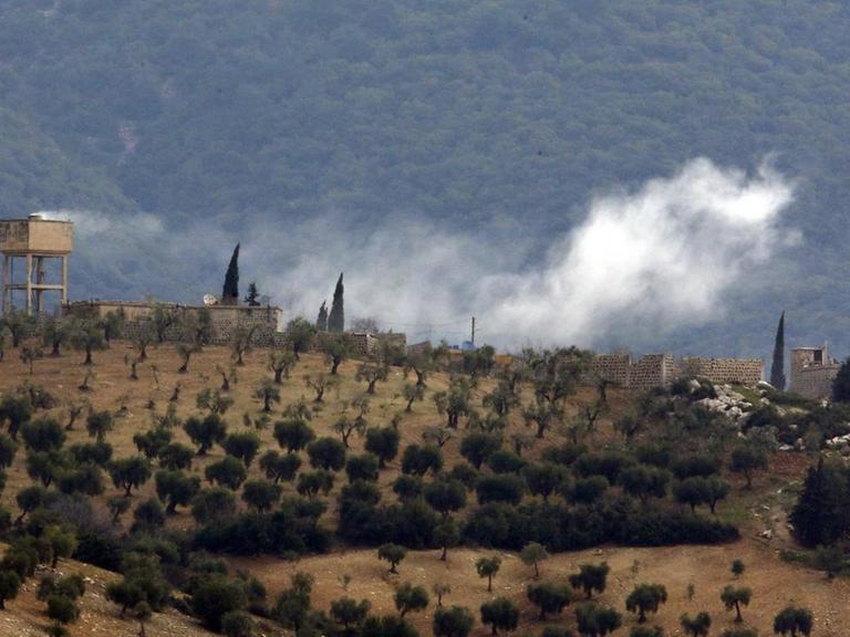 Das Bild zeigt Rauch, der über einer hügeligen Landschaft im Nordwesten Syriens nach Artilleriebeschuss durch die türkische Armee aufsteigt.