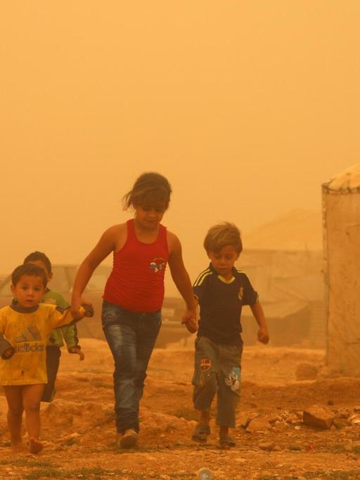 Zu sehen sind drei Kinder in einem Flüchtlingslager bei Baalbek im Libanon, die Luft ist wegen eines Sandsturms gelb.