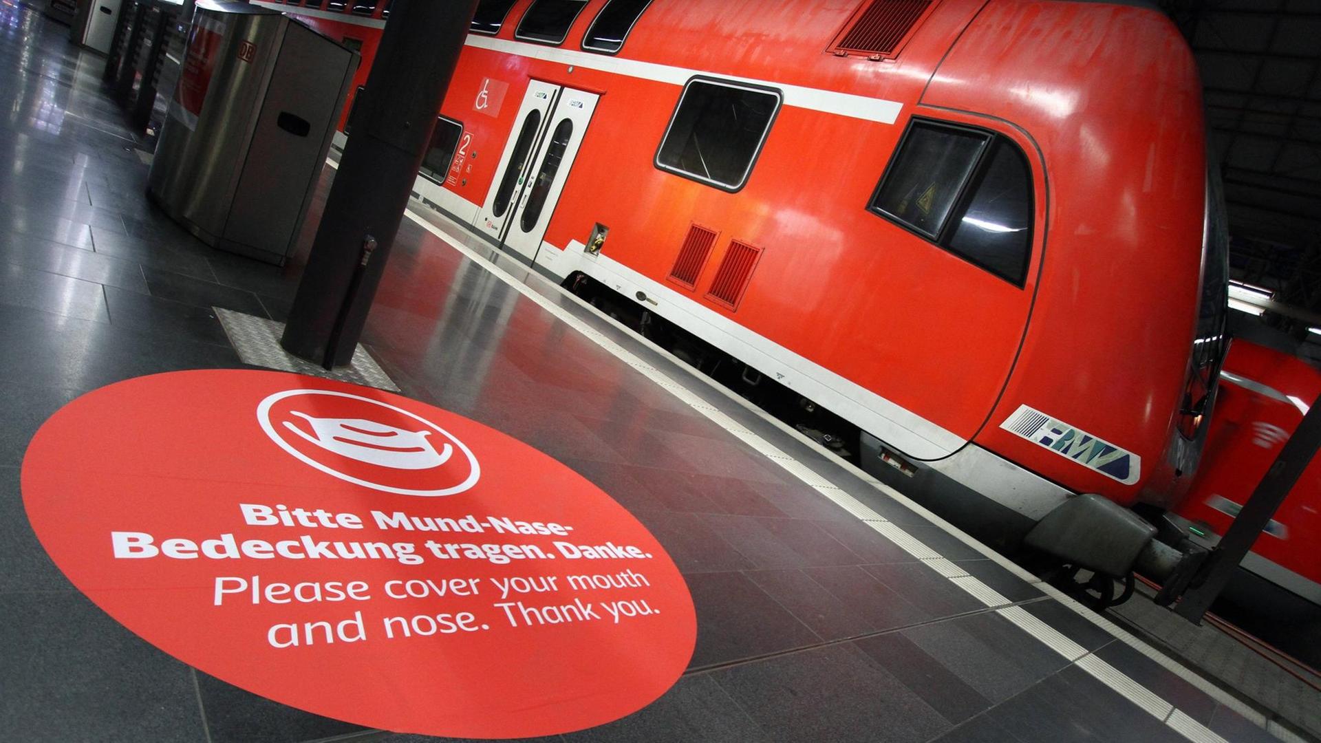 Aufkleber mit Piktogramm und Aufschrift "Bitte Mund-Nase-Bedeckung tragen" auf dem Fußboden eines Bahnsteigs vor einem Regionalexpress der Deutschen Bahn. Aufkleber mit Piktogramm und Aufschrift "Bitte Mund-Nase-Bedeckung tragen" auf dem Fußboden eines Bahnsteigs vor einem Regionalexpress der Deutschen Bahn.
