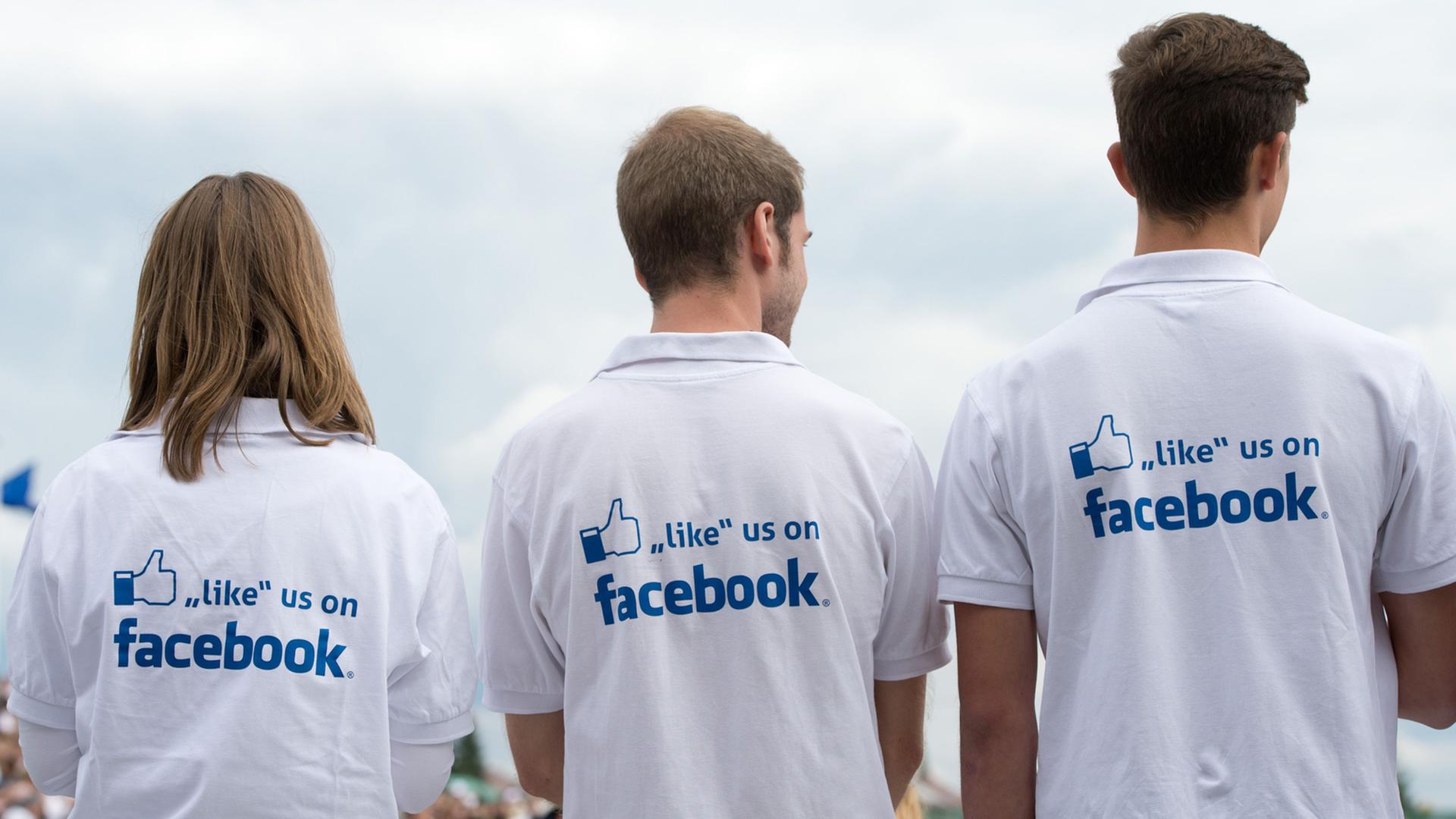 Drei Jugendliche tragen T-Shirts mit der Aufschrift "like us on Facebook" auf dem Rücken. 
