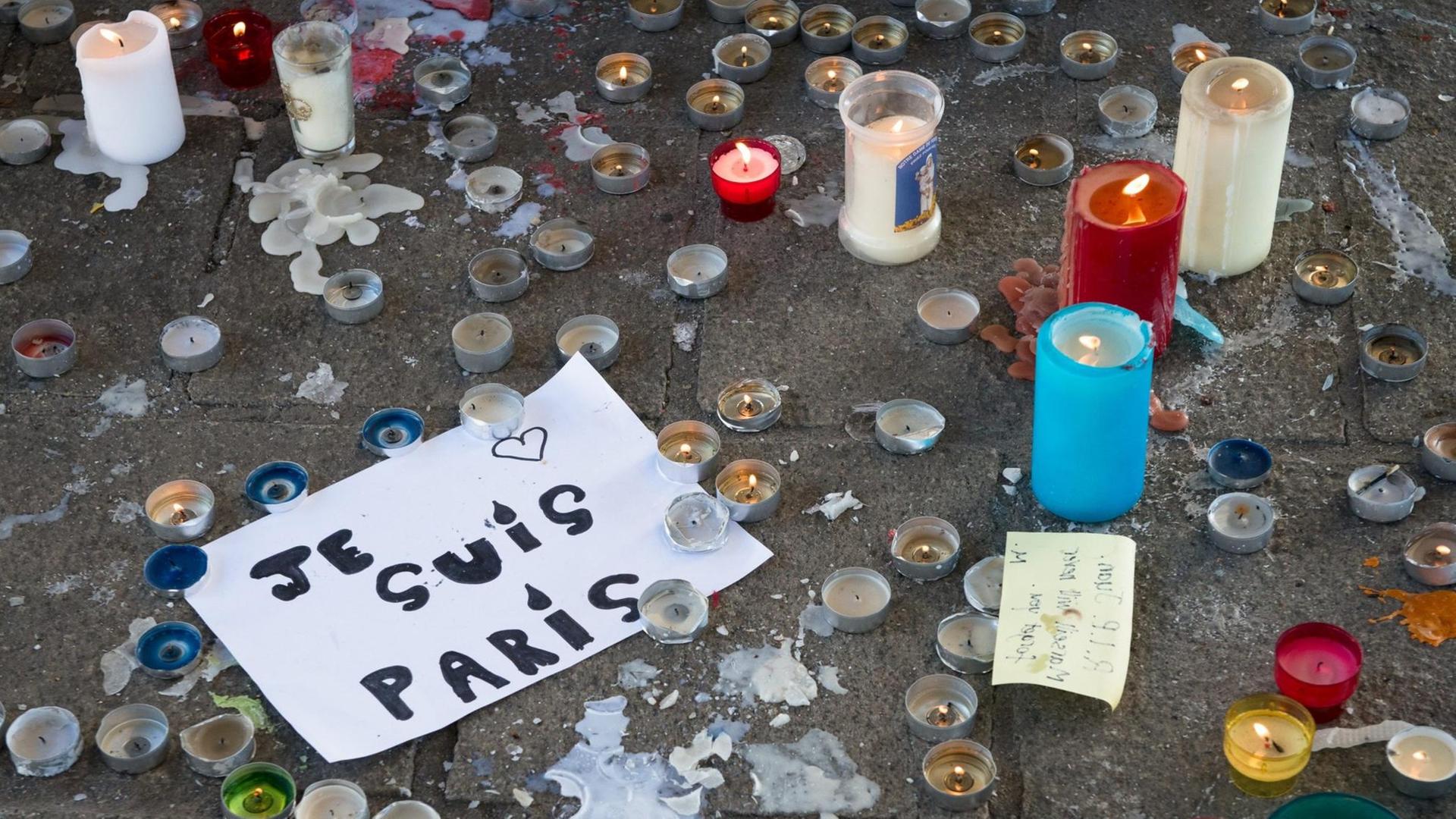 Zu sehen sind viele Teelichter, und der Schriftzug "Je suis Paris" auf einem Blatt Papier. Zu sehen sind viele Teelichter, und der Schriftzug "Je suis Paris" auf einem Blatt Papier.