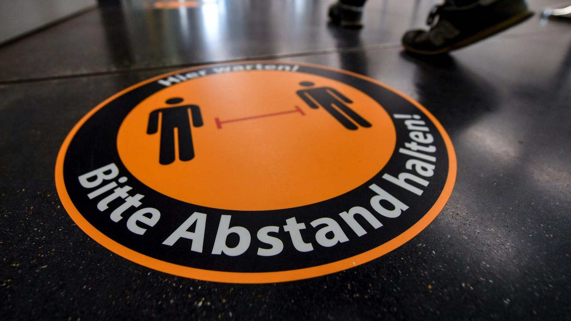 Auf dem Boden eines Museums klebt ein großes rundes Schild mit der Schrift: "Hier warten! Bitte Abstand halten" Auf dem Boden eines Museums klebt ein großes rundes Schild mit der Schrift: "Hier warten! Bitte Abstand halten"