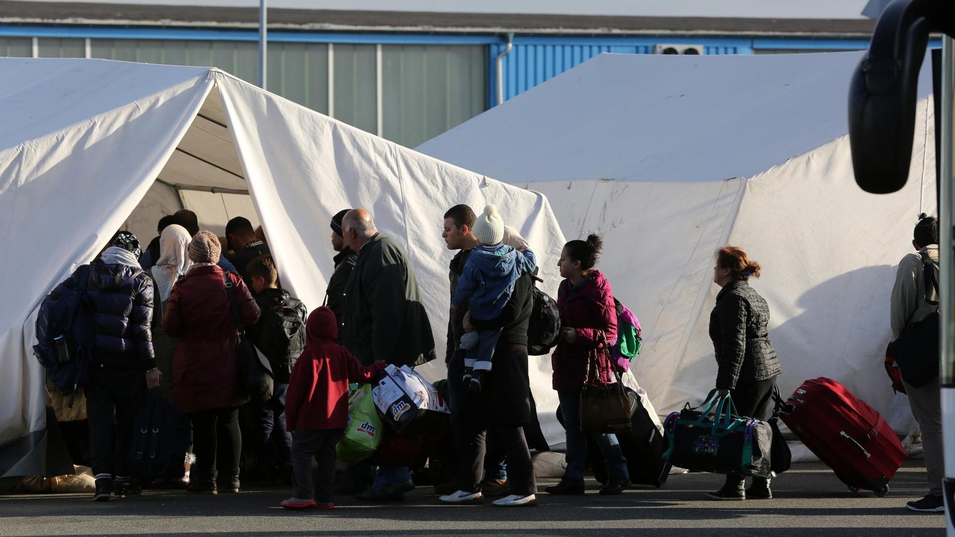 Flüchtlinge stehen in einer Schlange vor einem weißen Zelt an.
