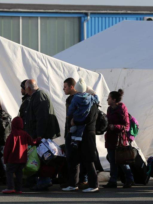 Flüchtlinge stehen in einer Schlange vor einem weißen Zelt an.