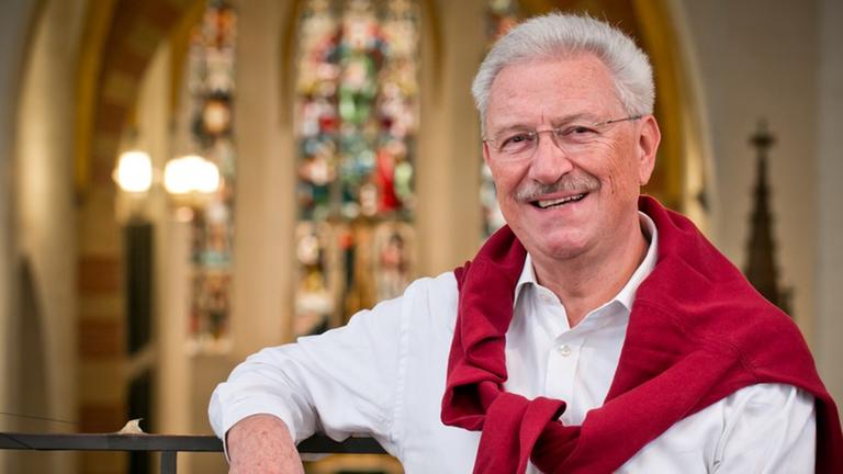 Der Sänger steht auf der Orgelempore einer Kirche mit bunten Glasfenstern und lächelt. Der Sänger steht auf der Orgelempore einer Kirche mit bunten Glasfenstern und lächelt.