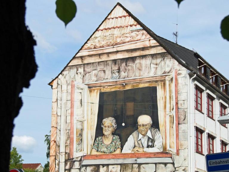 Ein Wandbild an einer Hausfassade in Bremen zeigt ein altes Ehepaar beim Blick aus dem Fenster auf den Rembertikreisel.