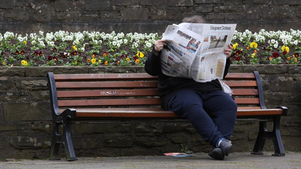 Eine Frau sitzt auf einer Bank und liest die "Siegener Zeitung".