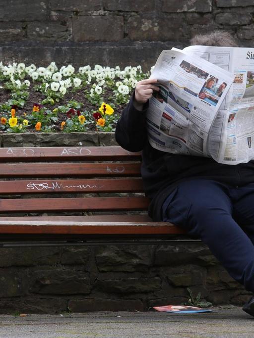Eine Frau sitzt auf einer Bank und liest die "Siegener Zeitung".