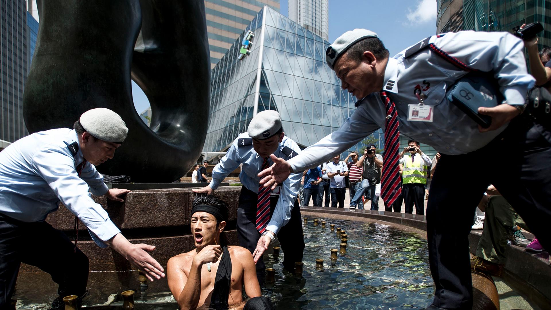Ein Mann von Occupy Central sitzt in einem Brunnen und drei Ordnungspersonen bitten ihn per Handzeichen diesen zu verlassen Ein Mann von Occupy Central sitzt in einem Brunnen und drei Ordnungspersonen bitten ihn per Handzeichen diesen zu verlassen