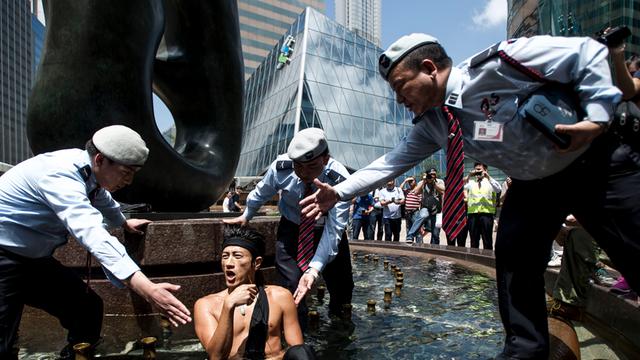 Ein Mann von Occupy Central sitzt in einem Brunnen und drei Ordnungspersonen bitten ihn per Handzeichen diesen zu verlassen