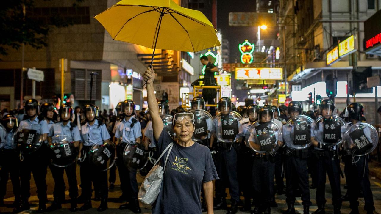 Eine Frau steht mit dem Rücken zu einer Hongkonger Polizeieinheit gewandt und hält ihren gelben Regenschirm in die Höhe.