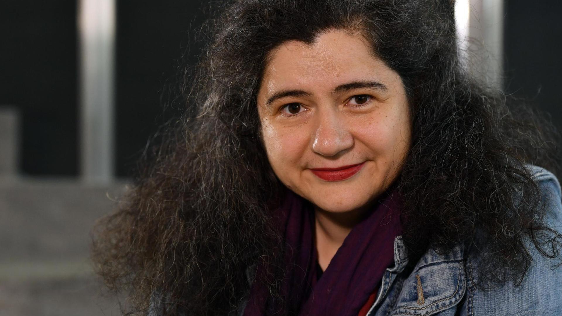 Eine Frau mit dunklen Locken lächelt in die Kamera. Eine Frau mit dunklen Locken lächelt in die Kamera.