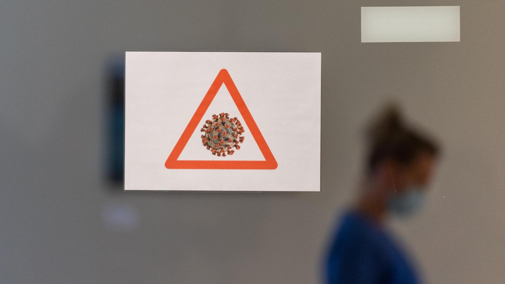 Eine Gesundheits- und Krankenpflegerin läuft auf der Corona-Station im Städtischen Klinikum Dresden in Schutzausrüstung hinter einer Scheibe an der ein Achtungssymbol mit einem stilisierten Cornavirus angebracht ist vorbei. Eine Gesundheits- und Krankenpflegerin läuft auf der Corona-Station im Städtischen Klinikum Dresden in Schutzausrüstung hinter einer Scheibe an der ein Achtungssymbol mit einem stilisierten Cornavirus angebracht ist vorbei.