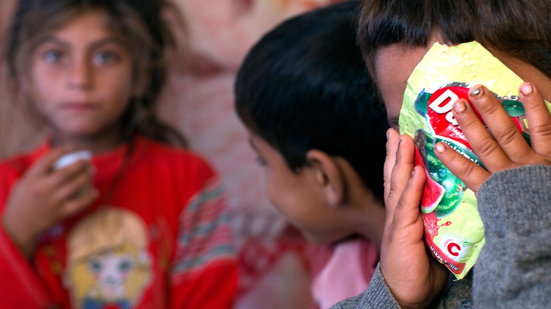 Drei Kinder einer syrischen Flüchtlingsfamilie, eines verdeckt sein Gesicht mit einer Tüte Bonbons. Drei Kinder einer syrischen Flüchtlingsfamilie, eines verdeckt sein Gesicht mit einer Tüte Bonbons.