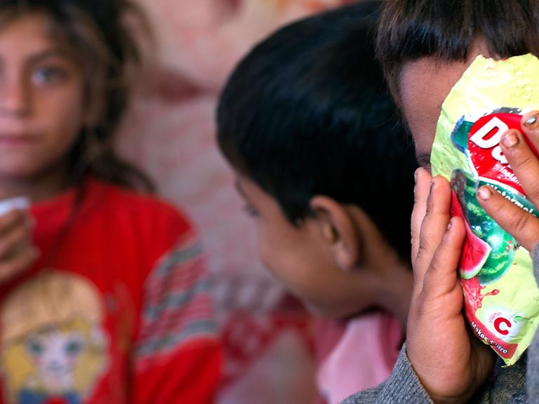 Drei Kinder einer syrischen Flüchtlingsfamilie, eines verdeckt sein Gesicht mit einer Tüte Bonbons.