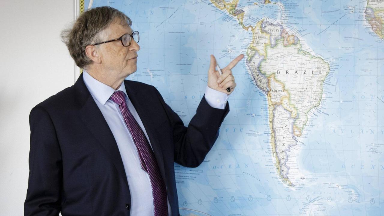 Bill Gates vor einer Karte Südamerikas. Mit dem Finger zeigt er auf Ecuador.