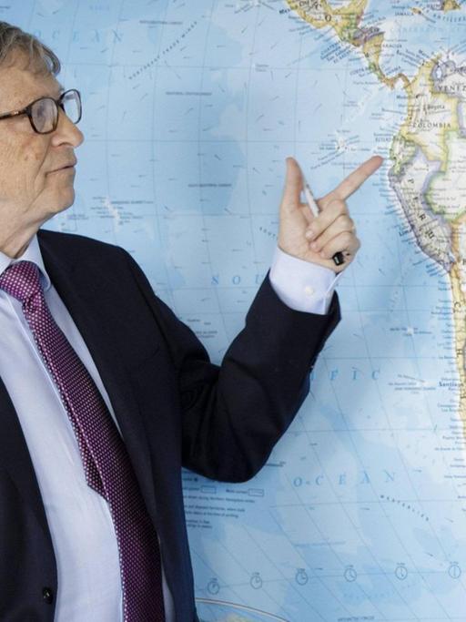 Bill Gates vor einer Karte Südamerikas. Mit dem Finger zeigt er auf Ecuador.