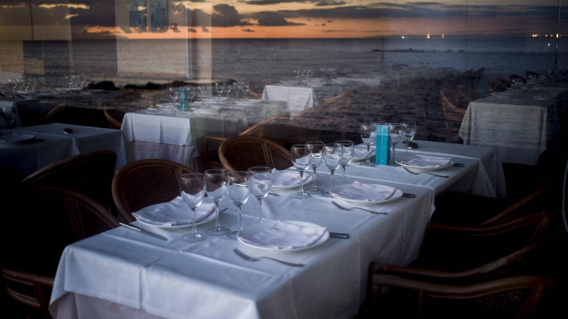 Leere Tische in einem Restaurant, in den Fensterscheiben spiegelt sich die Küste. Leere Tische in einem Restaurant, in den Fensterscheiben spiegelt sich die Küste.