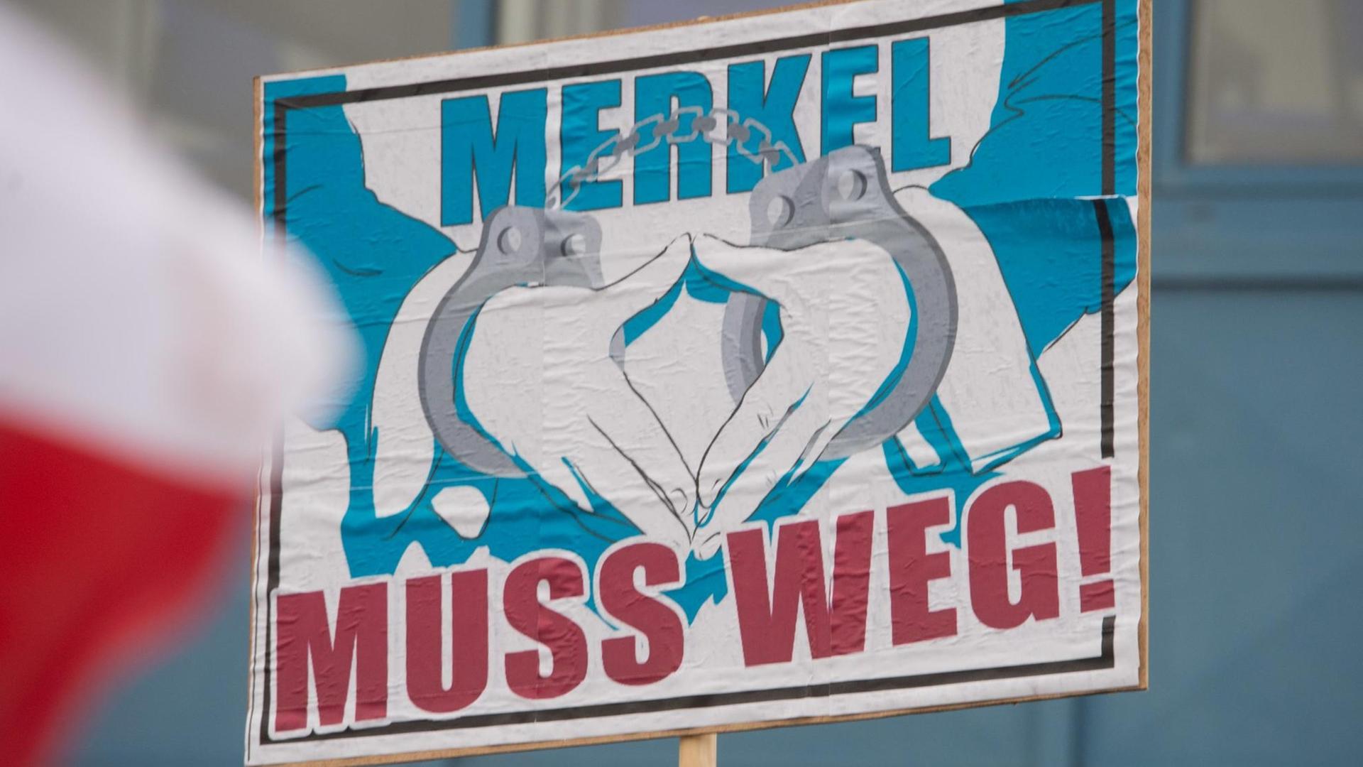 Ein Plakat mit der Aufschrift "Merkel muss weg" und eine mit zwei Händen geformte Raute Ein Plakat mit der Aufschrift "Merkel muss weg" und eine mit zwei Händen geformte Raute
