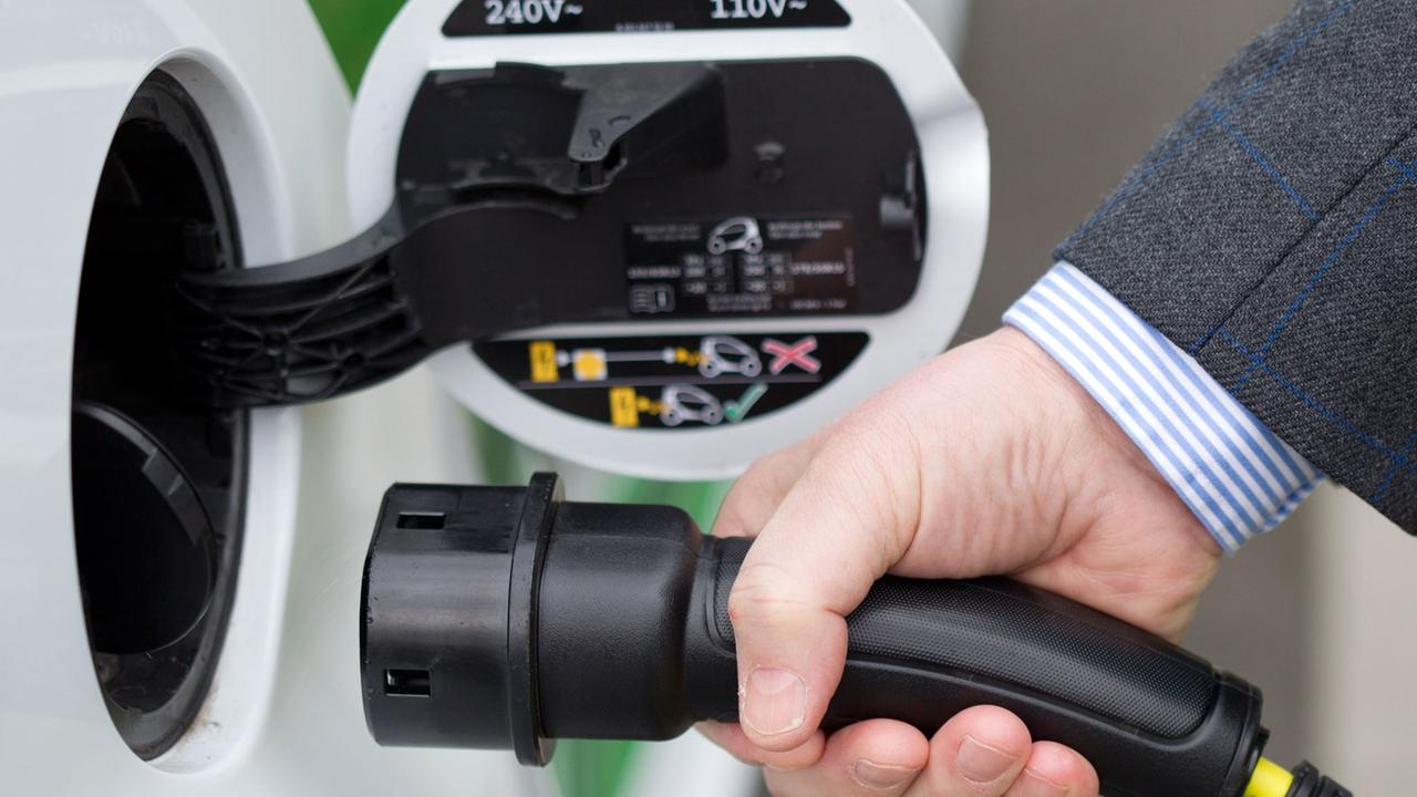 Ein Autofahrer steckt einen Ladestecker einer E-Mobilität-Zapfsäule in ein batteriebetriebenes Fahrzeug. Ein Autofahrer steckt einen Ladestecker einer E-Mobilität-Zapfsäule in ein batteriebetriebenes Fahrzeug.