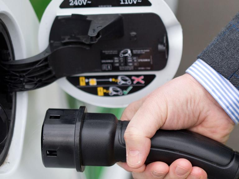 Ein Autofahrer steckt einen Ladestecker einer E-Mobilität-Zapfsäule in ein batteriebetriebenes Fahrzeug.