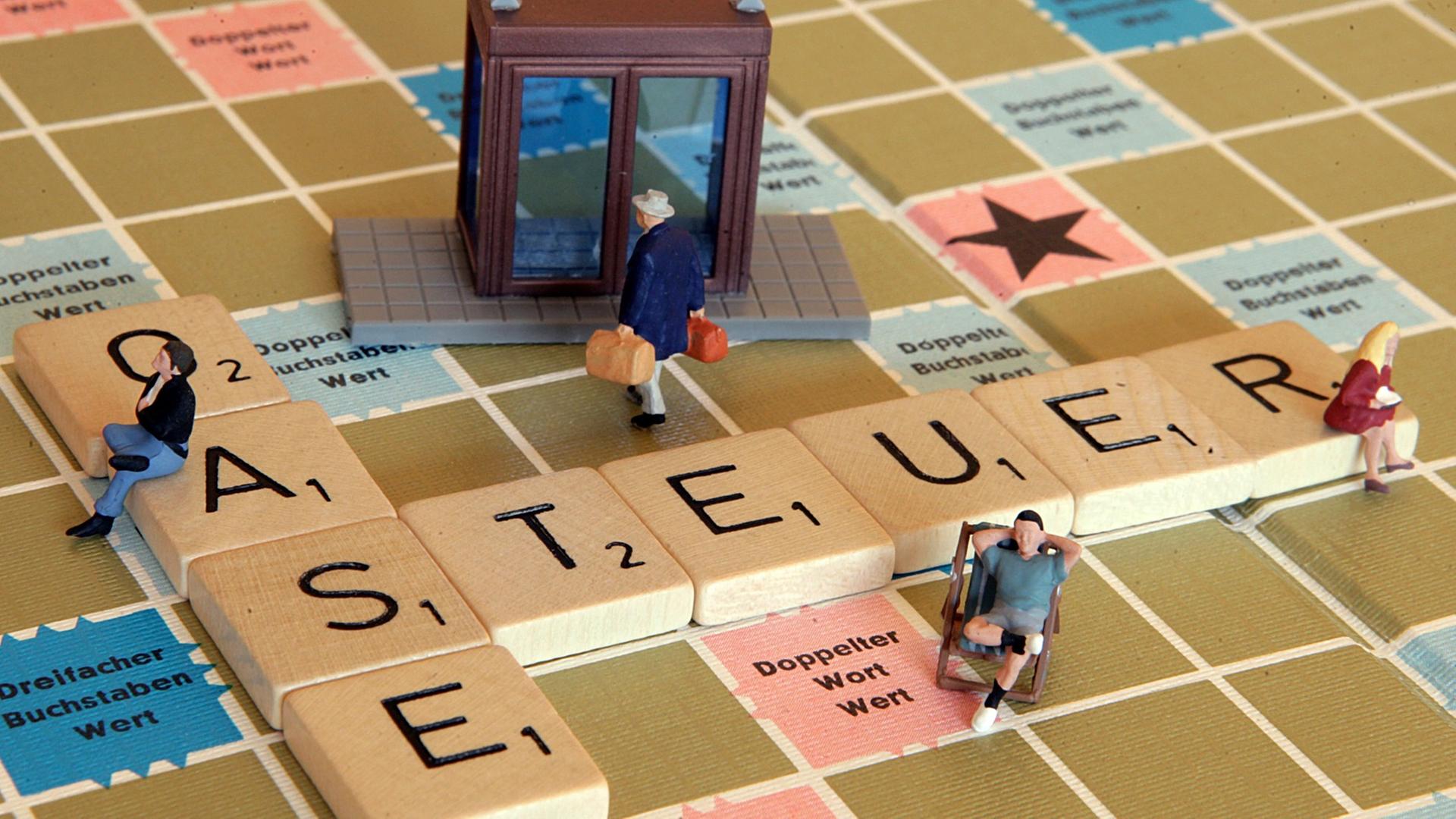 Eine Miniaturfigur trägt zwei Geldkoffer auf einem Scrabble-Spiel in eine Bank (Illustration), auf dem das Wort Steueroase liegt. Eine Miniaturfigur trägt zwei Geldkoffer auf einem Scrabble-Spiel in eine Bank (Illustration), auf dem das Wort Steueroase liegt.