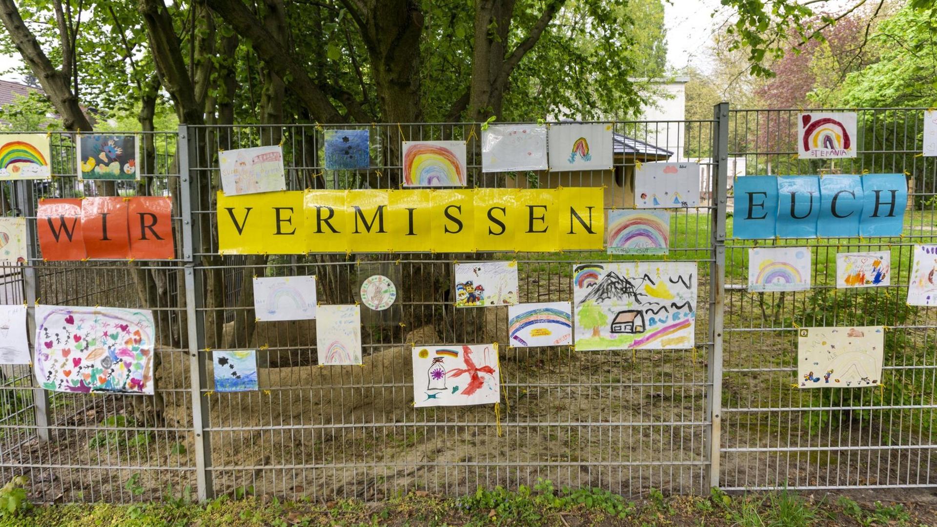 Am Zaun eines Kindergartens hängen Bilder und ein Schild mit der Aufschrift: Wir vermissen euch. Am Zaun eines Kindergartens hängen Bilder und ein Schild mit der Aufschrift: Wir vermissen euch.