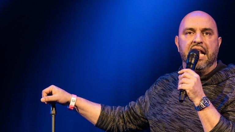Der Kabarettist Serdar Somuncu steht auf einer dunklen Bühne Der Kabarettist Serdar Somuncu steht auf einer dunklen Bühne