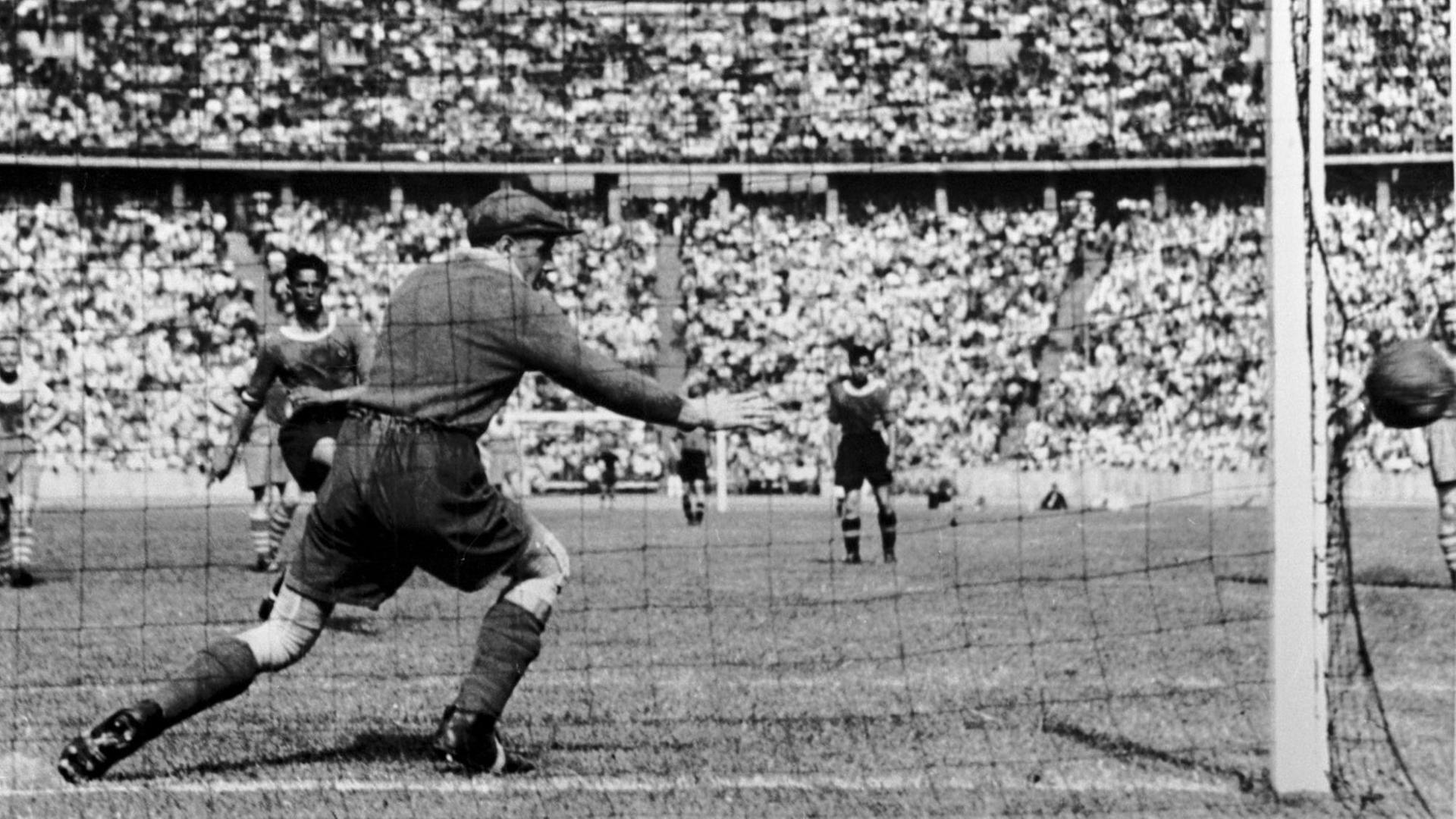 Blick auf ein Tor von hinten. Man sieht wie der Ball im Tor landet und der Torwart sich noch in die Richtung des Balles streckt. Der Torwart trägt eine Schiebermütze. (Historische Fotografie) Blick auf ein Tor von hinten. Man sieht wie der Ball im Tor landet und der Torwart sich noch in die Richtung des Balles streckt. Der Torwart trägt eine Schiebermütze. (Historische Fotografie)