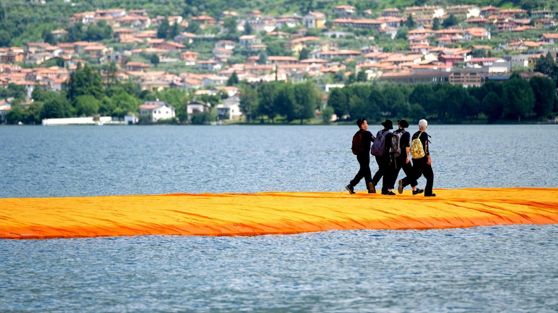 Menschen gehen am 17.06.2016 über orangefarbene, schwimmenden Stege im Rahmen des Projekts "The Floating Piers" von Christo auf dem Lago d'Iseo in Italien. Menschen gehen am 17.06.2016 über orangefarbene, schwimmenden Stege im Rahmen des Projekts "The Floating Piers" von Christo auf dem Lago d'Iseo in Italien.