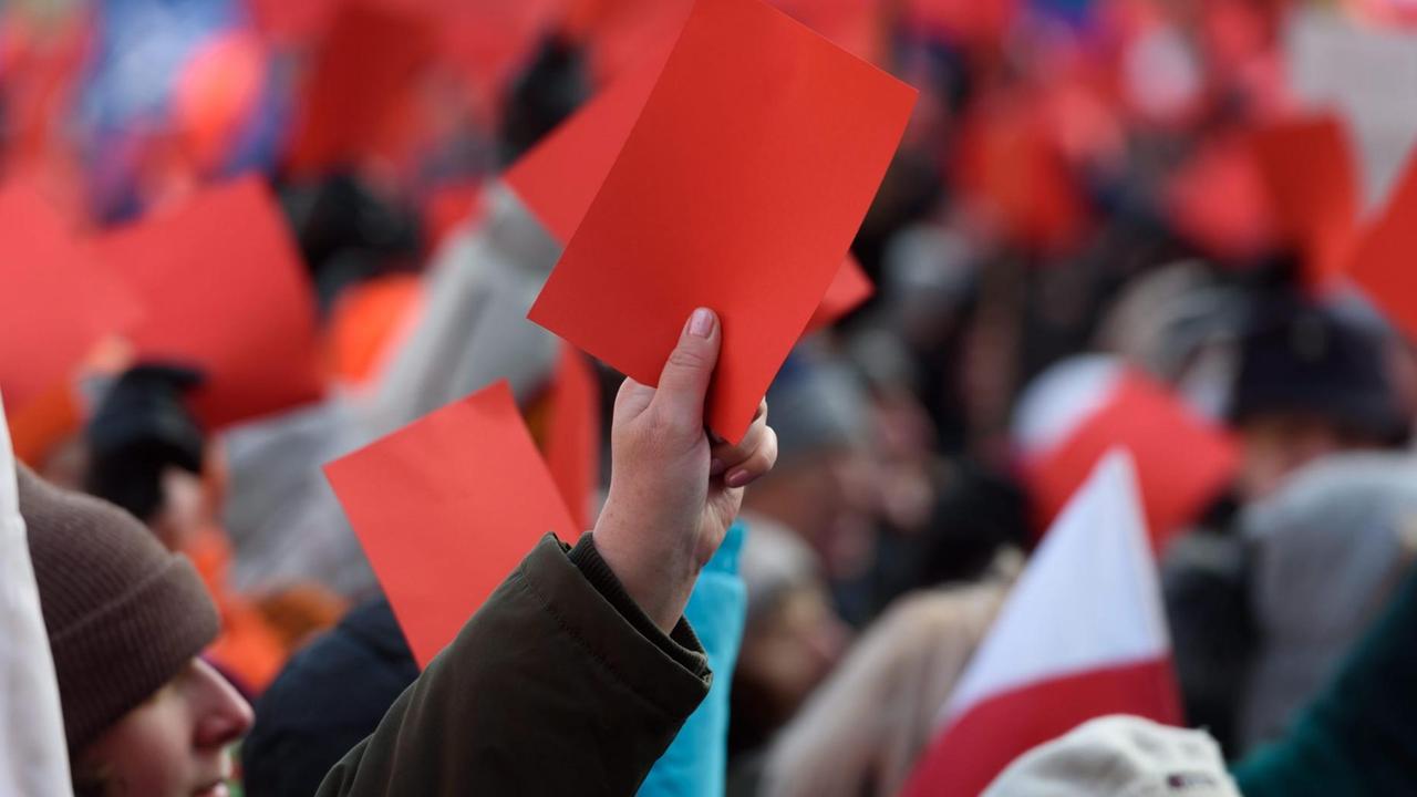 Tausende Polen demonstrieren gegen neue Gesetze mit roten Karten in den Händen.