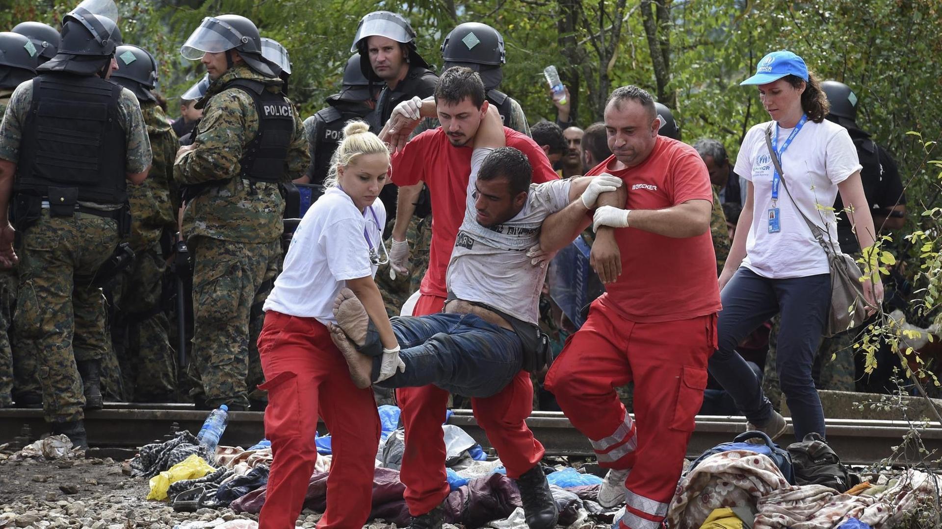 Sanitäter helfen einem kollabierten Mann an der Grenze zu Mazedonien. Sanitäter helfen einem kollabierten Mann an der Grenze zu Mazedonien.