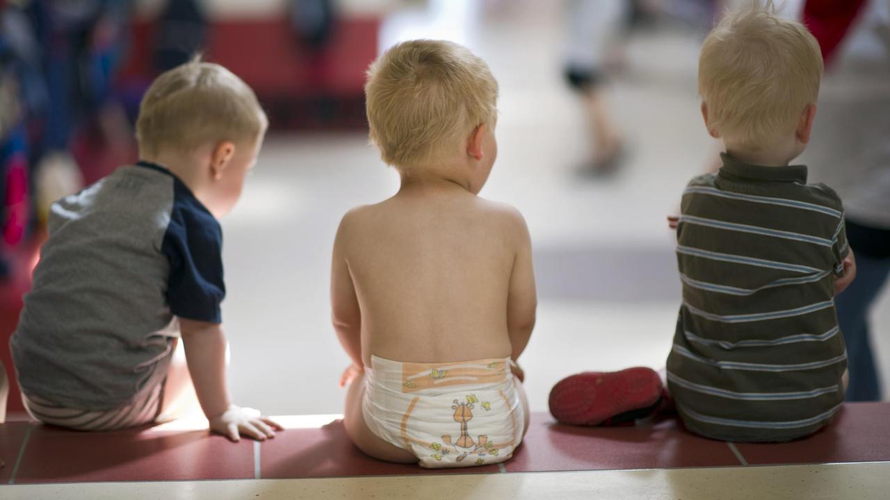 In einer Kindertageseinrichtung sitzen drei Kleinkinder auf einer Stufe