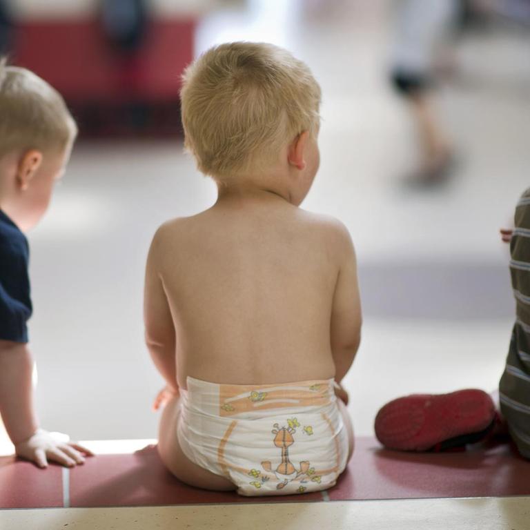 In einer Kindertageseinrichtung sitzen drei Kleinkinder auf einer Stufe