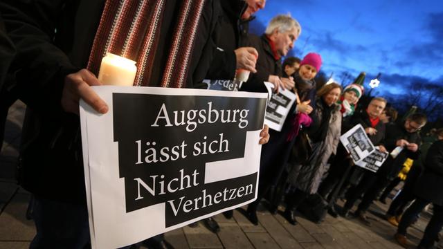 "Augsburg lässt sich Nicht Verhetzen" steht auf dem Plakat eines Mannes der am Königsplatz bei der Kranzniederlegung eines AfD-Abgeordneten gegen politische Instrumentalisierung demonstriert.