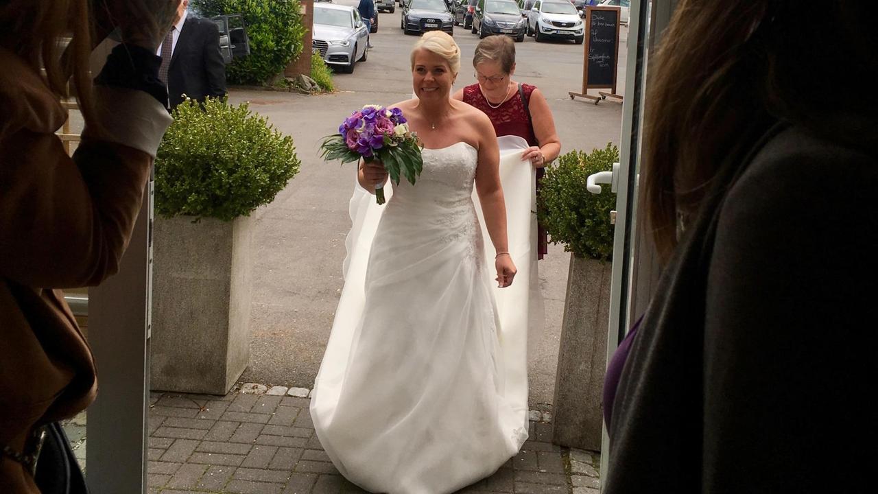 Eine Braut im weißen Kleid mit Schleppe tritt durch eine Tür Eine Braut im weißen Kleid mit Schleppe tritt durch eine Tür