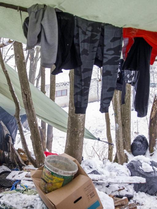 Zwei Flüchtlinge unter selbstgebauten Zeltplanen in einem verschneiten Wald