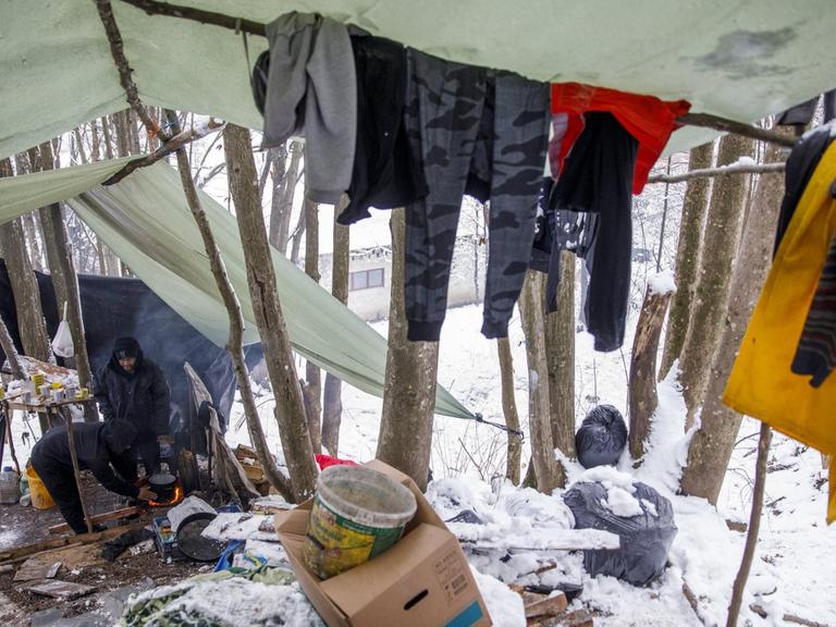 Zwei Flüchtlinge unter selbstgebauten Zeltplanen in einem verschneiten Wald