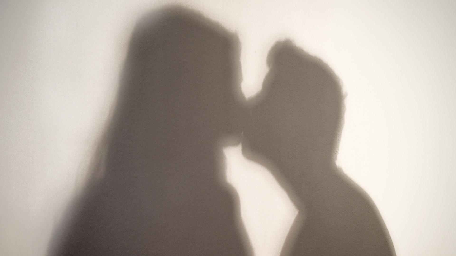 Der Schatten einer Frau und eines Mannes, die sich küssen, sind an eine Wand geworfen.