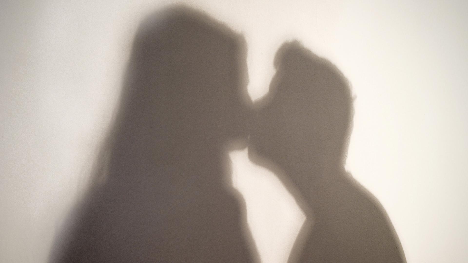 Der Schatten einer Frau und eines Mannes, die sich küssen, sind an eine Wand geworfen. Der Schatten einer Frau und eines Mannes, die sich küssen, sind an eine Wand geworfen.