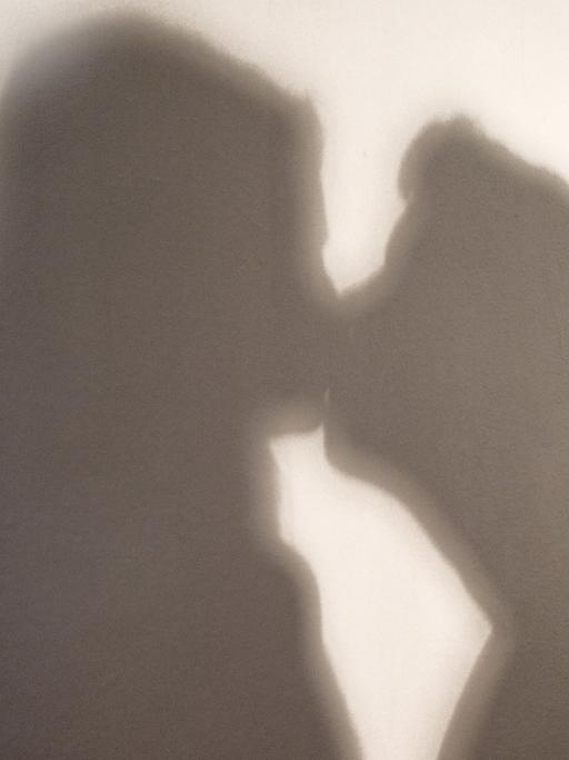 Der Schatten einer Frau und eines Mannes, die sich küssen, sind an eine Wand geworfen.