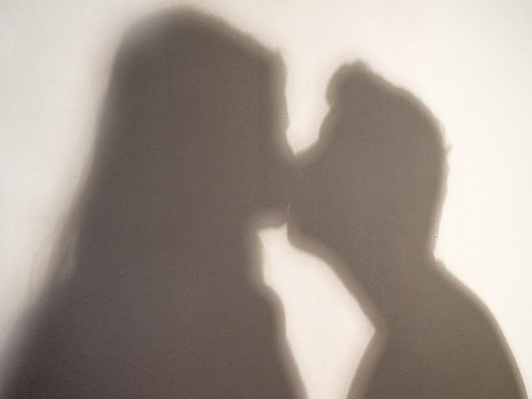 Der Schatten einer Frau und eines Mannes, die sich küssen, sind an eine Wand geworfen.