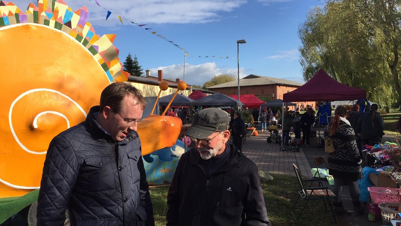 Zwei Penzliner Stadträte stehen auf einem Herbstfest vor einer orangefarbenen Schnecke aus Pappmaché.