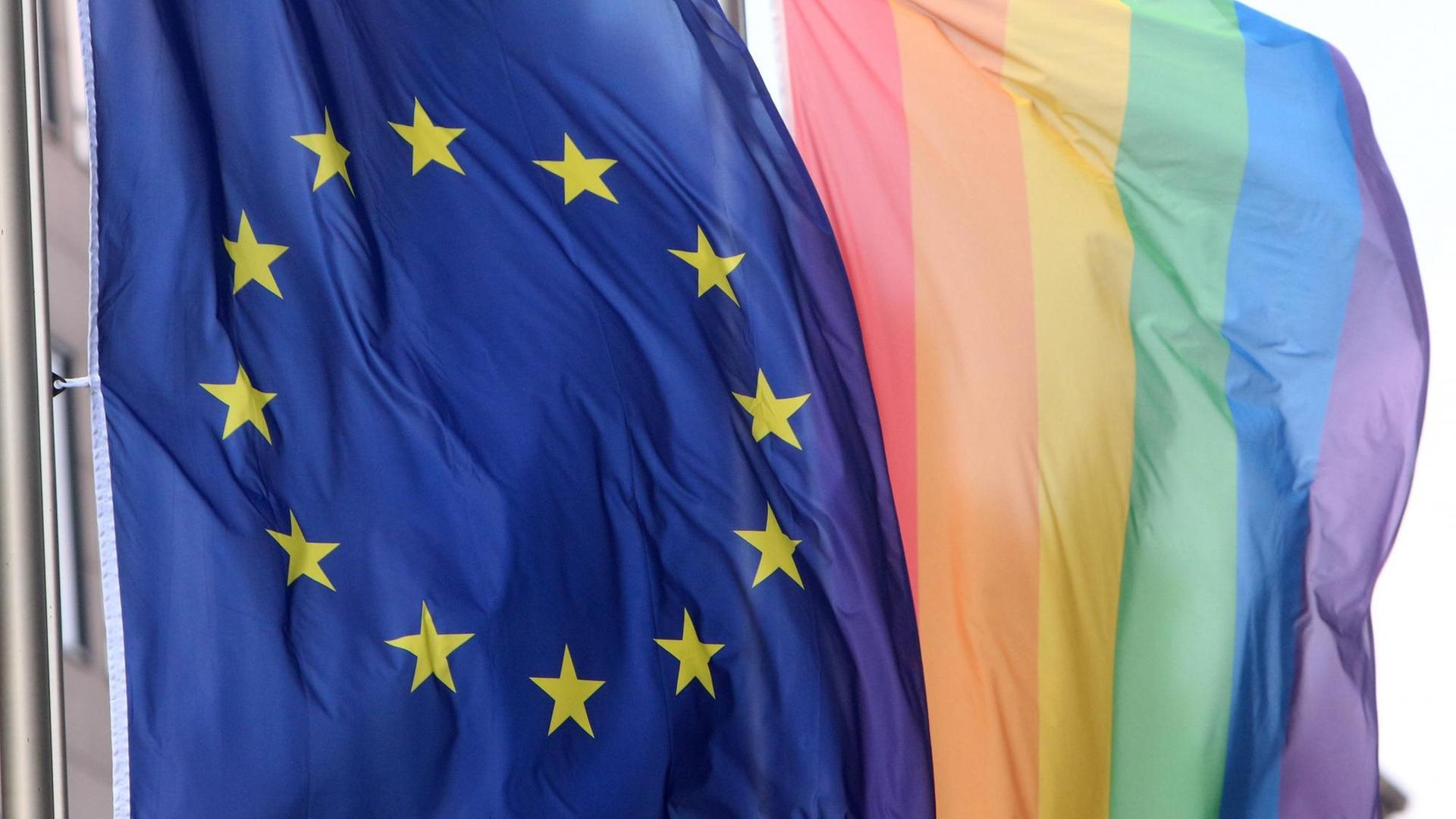 Eine Flagge der Europäischen Union weht neben einer Regenbogenflagge.