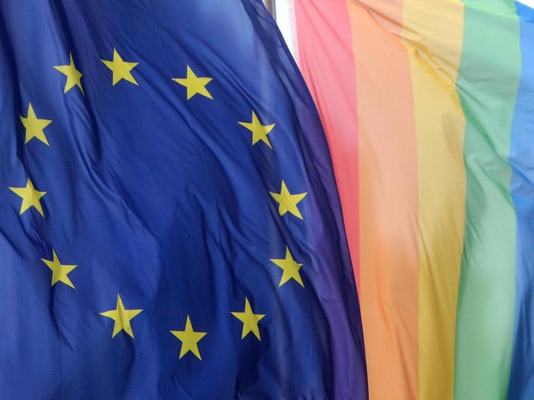 Eine Flagge der Europäischen Union weht neben einer Regenbogenflagge.
