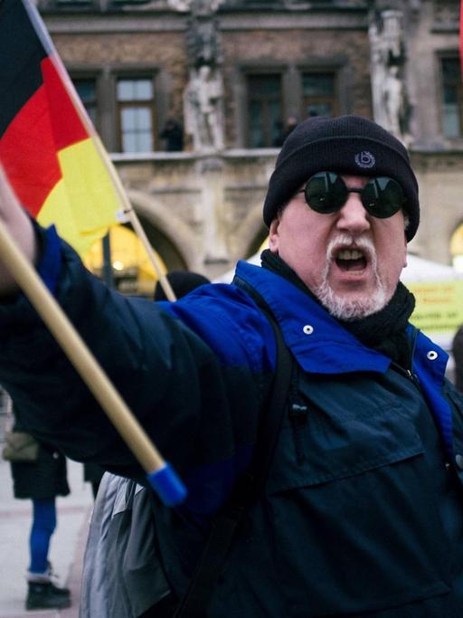 Ein vermummter Pegida-Demonstrant schwenkt eine Deutschland-Fahne.