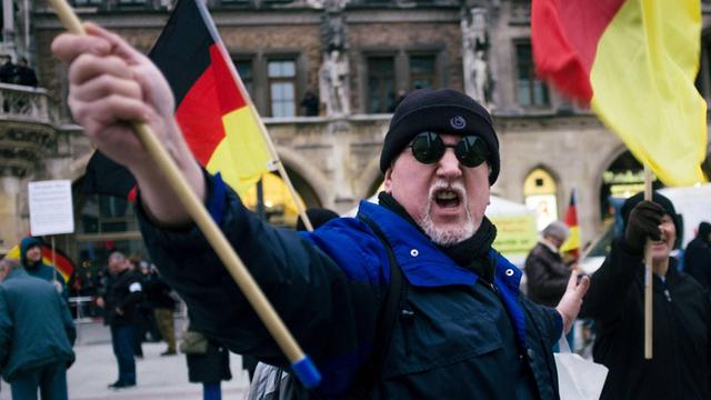 Ein vermummter Pegida-Demonstrant schwenkt eine Deutschland-Fahne.
