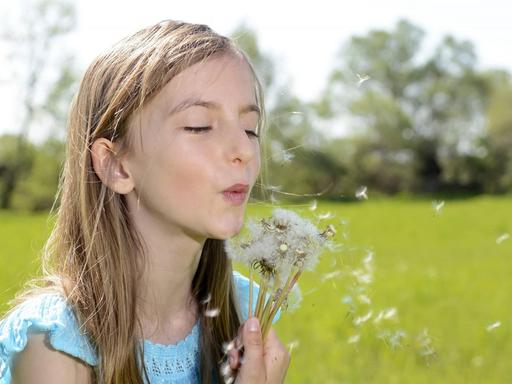 Ein blondes Mädchen steht mit einer Pusteblume auf einem Feld